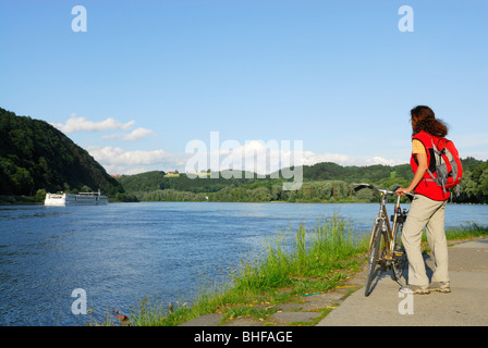 Ciclista femmina che guarda sul fiume Danubio, Danubio Percorso Ciclabile Passau a Vienna, Passau, Bassa Baviera, Germania Foto Stock