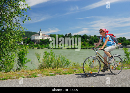 Ciclista femmina a cavallo lungo il fiume Danubio, Persenbeug castello in background, Danubio Percorso Ciclabile Passau a Vienna, Persenbeug, Lowe Foto Stock