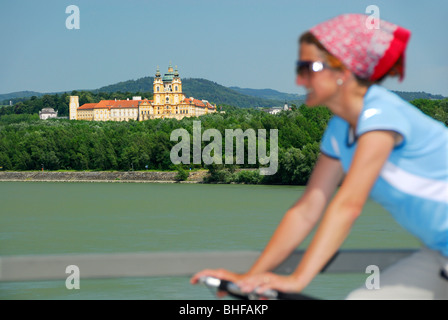 Ciclista femmina a cavallo lungo il fiume Danubio, l'Abbazia di Melk in background, Danubio Percorso Ciclabile Passau a Vienna, Wachau, Austria inferiore, Foto Stock