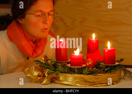 Donna soffiando fuori quattro candele a corona di Avvento Foto Stock
