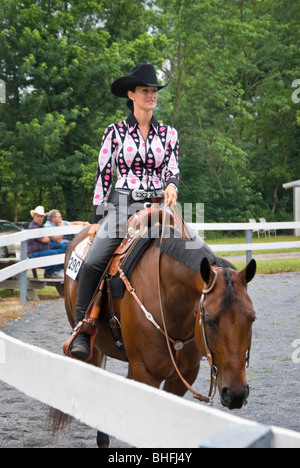 Immagine della donna graziosa western piacere a cavallo lungo la recinzione a rampa in uno spettacolo di cavalli anello. Foto Stock