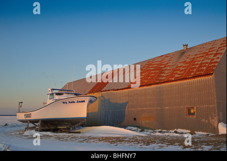 Lobster Boat al di fuori dell'acqua oltre la pesca shack sulla congelati Miramichi Bay in Canada con campo spazzate dal vento Foto Stock