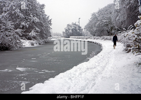 Un uomo cammina il suo cane attraverso la neve lungo il lato di una congelati Bridgewater Canal Foto Stock