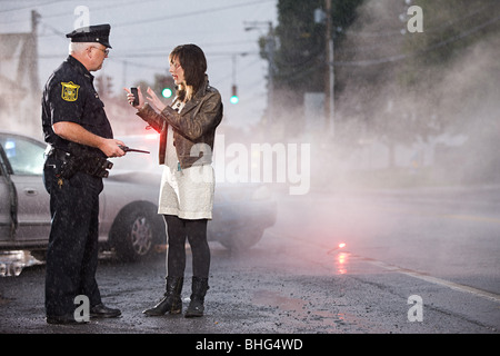 Giovane donna e funzionario di polizia a scena di crash Foto Stock