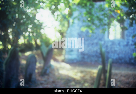 Vista impressioniste di archetipo inglese flint chiesa e cimitero con lapidi e pezzata luce delle foglie retroilluminato Foto Stock