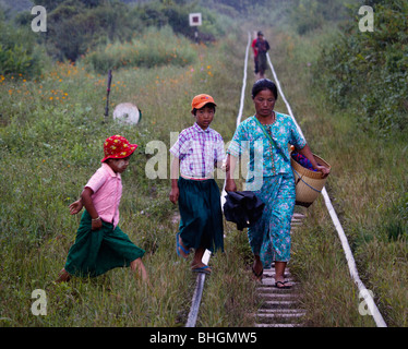 Una donna con i suoi due figli a piedi lungo una rampa ammaccato via la stazione ferroviaria sotto la pioggia, nel nord est del Myanmar Foto Stock