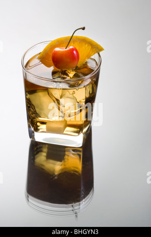In vecchio stile bevanda miscelata con fetta di arancia, ciliegia e zolletta di zucchero guarnire su uno sfondo grigio con la riflessione Foto Stock