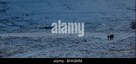 Quattro persone che camminano sulla strada innevata al tramonto su Blorenge moorland in inverno Wales UK Foto Stock