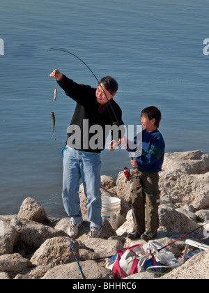 Un Asiatico-americano di padre e con il Figlio suo occhio una cattura di due di pesci di Tilapia nel sud della California's Salton Sea. Foto Stock