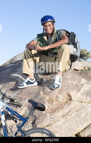 Uomo si siede sulla roccia che indossa il casco in bicicletta Foto Stock