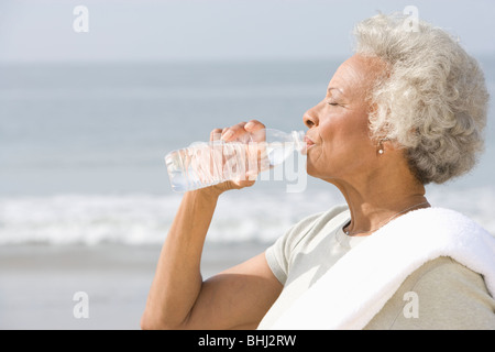 Senior donna stand con bevande acqua con un asciugamano sopra la sua spalla sulla spiaggia Foto Stock