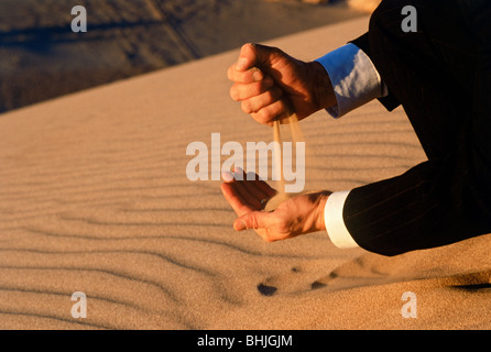 Uomo in business suit colata di deserto di sabbia attraverso le sue mani che simboleggiano il tempo calcolato e modificare e investimenti Foto Stock