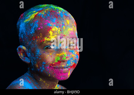 Felice giovane ragazzo indiano coperto di polvere colorata pigmento contro uno sfondo nero Foto Stock