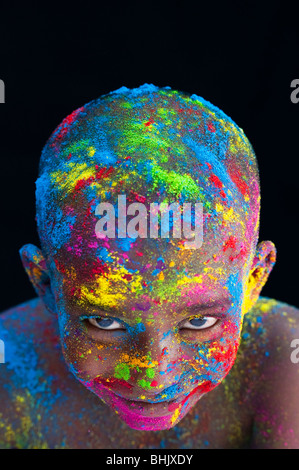 Felice giovane ragazzo indiano coperto di polvere colorata pigmento contro uno sfondo nero Foto Stock