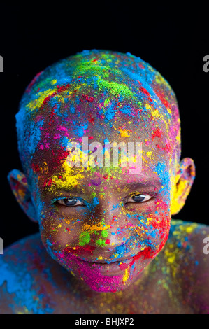 Felice giovane ragazzo indiano coperto di polvere colorata pigmento contro uno sfondo nero Foto Stock