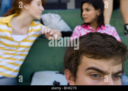 Alta scuola amici seduti insieme sulle gradinate, ragazzo guardando intensamente, Ragazze in Chat in background Foto Stock