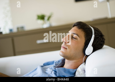 Giovane uomo rilassante sul divano ascolto di musica con cuffie