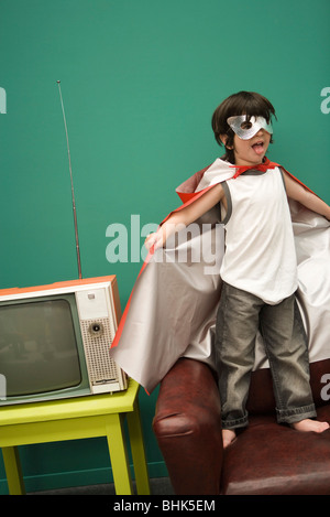 Ragazzo in costume da supereroe in piedi sul divano Foto Stock