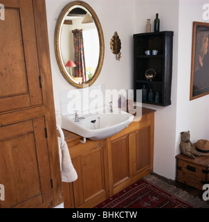 Specchio ovale suddetto bacino in legno montati vanity in piccole stanze da bagno di colore bianco con ripiani di antiquariato Foto Stock