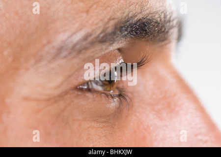 Close up di un giovane uomo dell'occhio che guarda lontano contro uno sfondo bianco Foto Stock