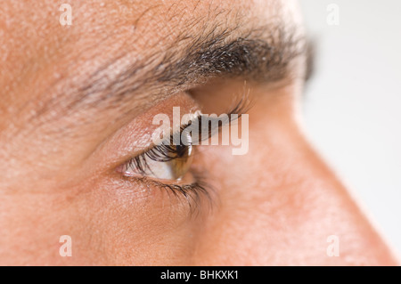 Close up di un giovane uomo dell'occhio che guarda lontano contro uno sfondo bianco Foto Stock