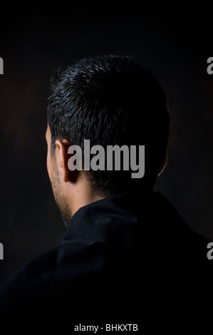 Vista posteriore del ritratto di un giovane uomo in piedi nel buio Foto Stock