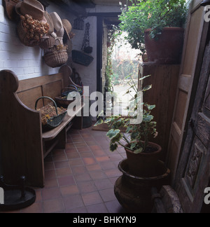 Vecchia chiesa di legno pew in stretto corridoio con pavimento in cotto e piastrelle houseplants verde Foto Stock