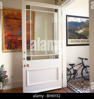 Semi-Bianco smaltato porta in sala tradizionale con grande pittura moderna sulla parete e porta aperta alla lobby di piccole dimensioni con bambino's bike Foto Stock