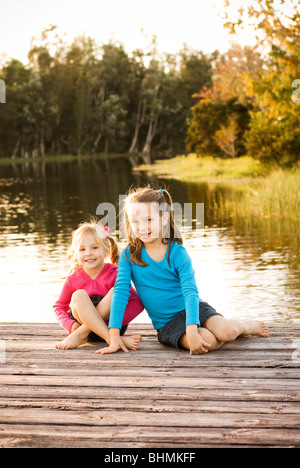 Piccole sorelle seduta sul lago di dock Foto Stock