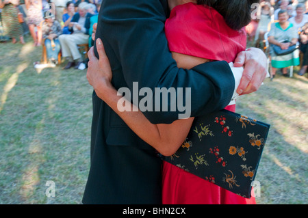 Un paio di abbracciare davanti a tutti gli ospiti ad un matrimonio all'aperto Foto Stock