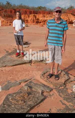 Due persone in piedi di orme di dinosauri in fossilizzato fango su una spiaggia vicino Broome Foto Stock