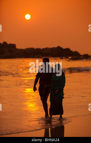 India Kerala, Kovalam, Faro (ADAM) spiaggia, Indiano giovane camminando lungo la riva al tramonto Foto Stock