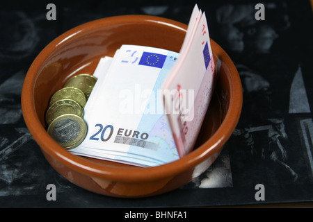 Le banconote e le monete in euro in un piatto su una pagina buia di un libro aperto Foto Stock