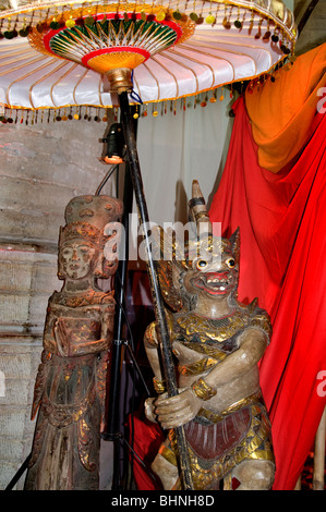 Due tradizionali statue balinesi in legno intagliate a mano, posizionate sotto un sacro ornamento a ombrello cerimoniale a più strati, Bali. Foto Stock