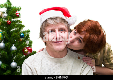 Donna matura baciando un vecchio marito vicino a un albero di Natale. Amorevole coppia senior isolati su sfondo bianco Foto Stock