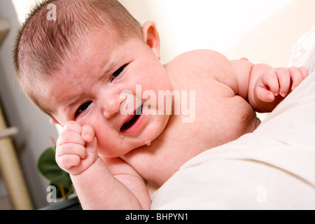 La faccia di un infelice unisex ispanica caucasica baby pianto con lacrime durante lo sfregamento occhio. Foto Stock