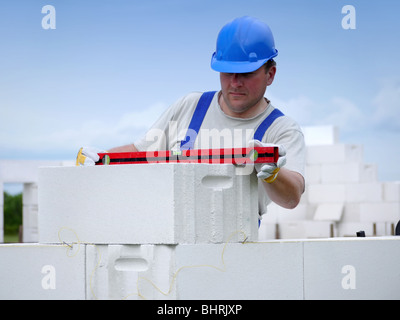 Mason controllo livello orizzontale del muro di casa strato essendo realizzato da aerato autoclavato blocchi in calcestruzzo Foto Stock