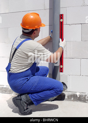 Plumber utilizza il livello per il controllo della linea di messa a piombo del pvc assemblato delle tubazioni di scarico all'interno di casa non finita Foto Stock