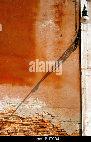 Ombra di lampione sul pastello sbiadito ocra rossa parete colorata a Venezia street, nel tardo pomeriggio Foto Stock