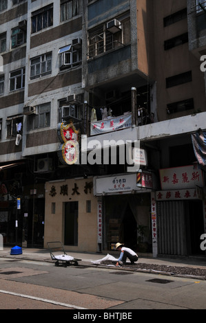 Ritratto di una donna in un bambù hat diffusione di frutti di mare al sole su un marciapiede fuori casa negozi, Queen's Road West, Hong Kong Foto Stock