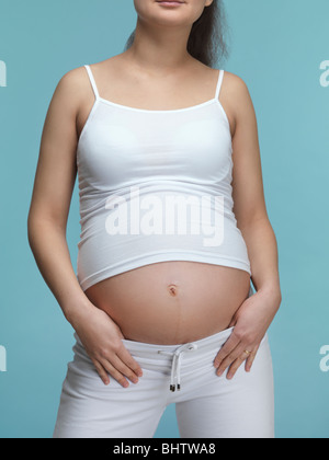 Giovane donna incinta in vestito bianco isolato su sfondo blu. Settimo mese di gravidanza. Foto Stock