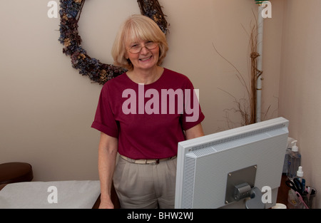 Questa sorridente e calda donna matura è un medico professionista lavoratore in un ufficio con la tecnologia. Foto Stock