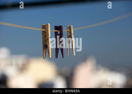 Tre pioli di vestiti appesi su una linea di lavaggio contro un luminoso blu del cielo sopra la città Foto Stock
