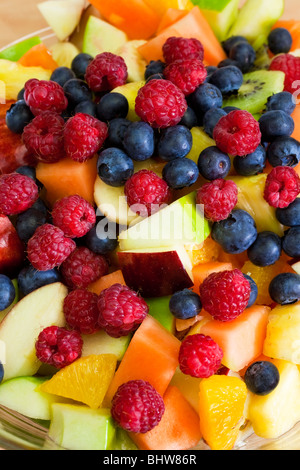 Close up di un recipiente contenente frutta fresca insalata di mirtilli, lamponi, melone, kiwi, mela, arancio e ananas Foto Stock