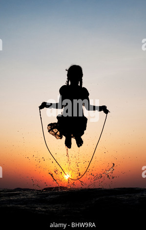 Silhouette di una giovane ragazza indiana saltando in acqua al tramonto. India Foto Stock