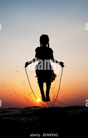 Silhouette di una giovane ragazza indiana saltando in acqua al tramonto. India Foto Stock