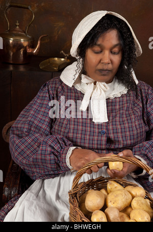Rievocazione storica scena di un nero cameriera vittoriano sbucciare le patate in una antica cucina Foto Stock
