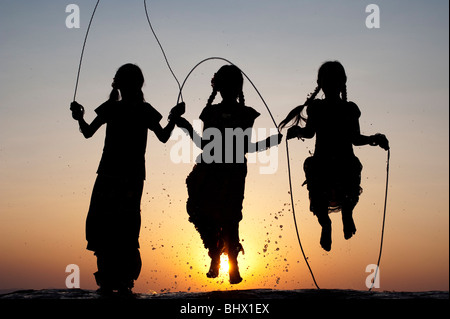 Silhouette di giovani ragazze indiano saltando in acqua al tramonto. India Foto Stock