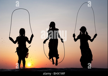 Silhouette di giovani ragazze indiano saltando in acqua al tramonto. India Foto Stock