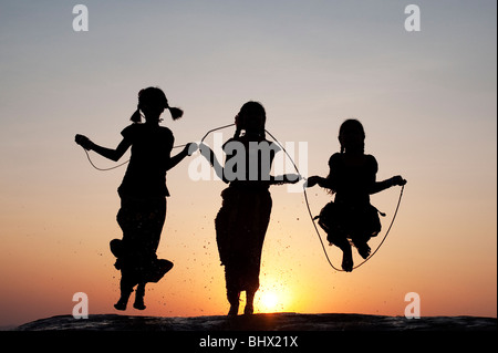 Silhouette di giovani ragazze indiano saltando in acqua al tramonto. India Foto Stock